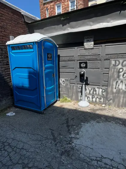 Blue porta potty in a paved alley beside a building under renovation