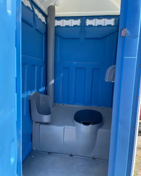 Inside a blue standard porta potty showing the seat, urinal and vent pipe